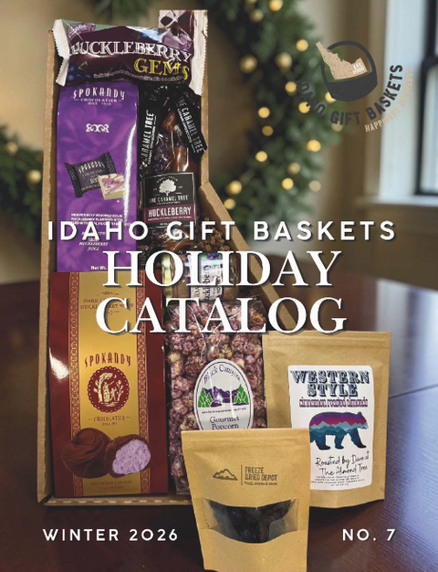 A holiday gift basket assortment displayed in a wooden box on a table, with packaged snacks and treats including Huckleberry Gems, Spoked Bay, and Western Style. Large text reads 'IDAHO GIFT BASKETS HOLIDAY CATALOG' with 'WINTER 2026' and 'NO7.